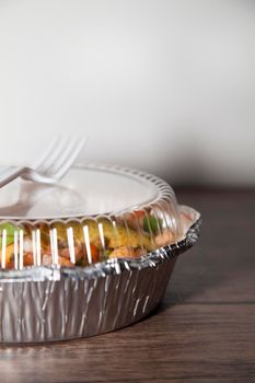 Ceviche in a tin carry out container with a white, plastic fork on top, on a wooden table and with a white background