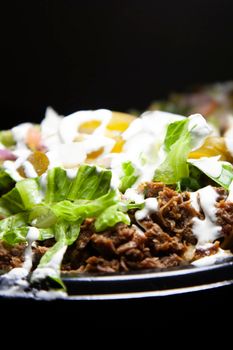 Nachos covered with shredded steak and lettuce, sliced jalapenos, sour cream, and diced tomato and onion