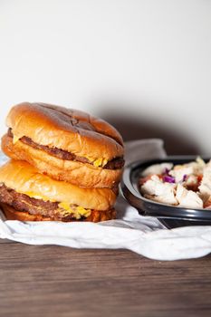 Two cheeseburgers stacked next to grilled chicken, bacon, lettuce, cabbage, shredded cheese, and diced tomato salad in a takeout container