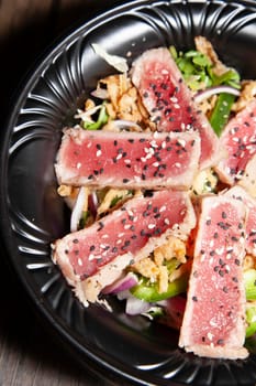 Seared tuna salad with lettuce, sliced green bell pepper, and red onion on a wooden table