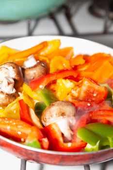 Sliced red, yellow, orange, and green bell peppers and whole portabella mushrooms in a frying pan