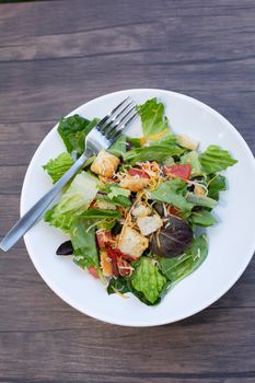 Salad of romaine lettuce, croutons, shredded cheddar cheese, and tomato on a white plate on a wooden table