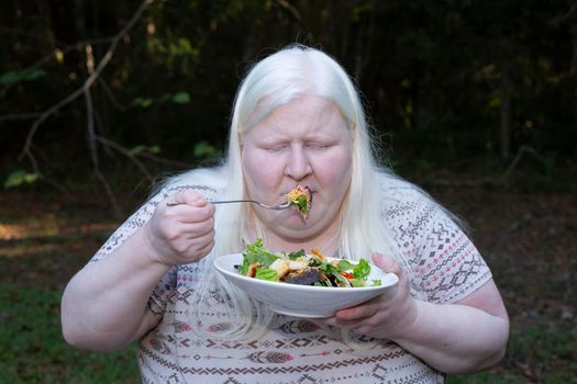 Woman eating a salad of romaine lettuce, croutons, shredded cheddar cheese, and tomato from a white plate