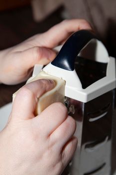 Woman using a large, metal cheese grater to shred white cheese on a white plate