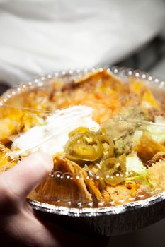 Woman grabbing a takeout tin of nachos with sour cream, chips, jalapenos, guacamole, and cheese