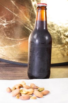 Almonds, cashews, pistachios, and peanuts on a tan cloth napkin on a wooden table with a beer in the background, with a golden tone