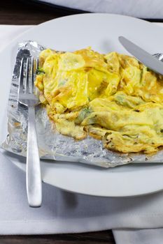 Vegetarian omlette with broccoli on silver foil on a white plate with silverware on a white napkin