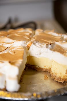 Lemon meringue pie missing a slice in its container on a stove