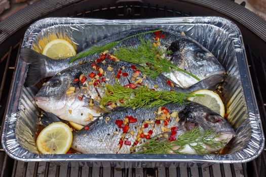 Sea bream in a dish with lemon and herbs, peppers on the barbecue