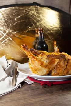 Whole roasted chicken on a white plate and a bottle of beer next to a grey napkin and silverware