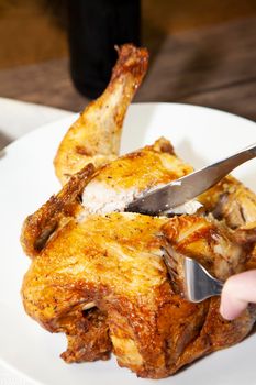 Woman cutting a large whole roasted chicken on a white plate with a beer in the background