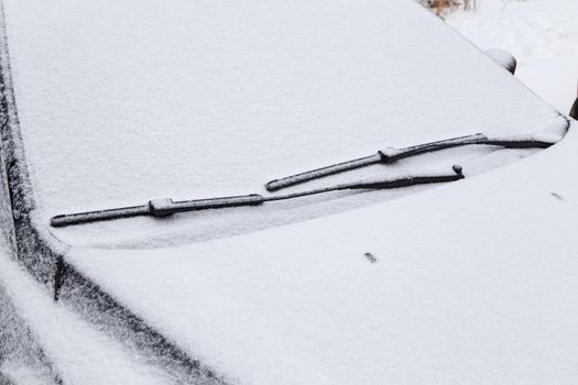 car windshield and wiper waterblades frozen and covered with snow at winter cloudy day light with selective focus and background blur