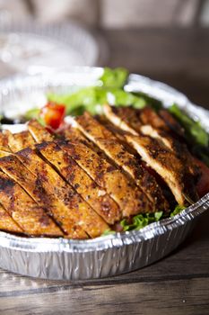 Roasted chicken breast sliced with lettuce and tomato in a foil container