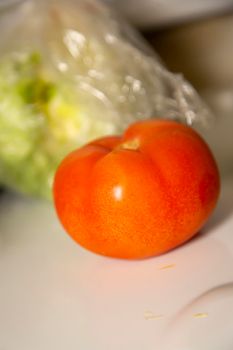 Uncut tomato in front of an out of focus head of lettuce