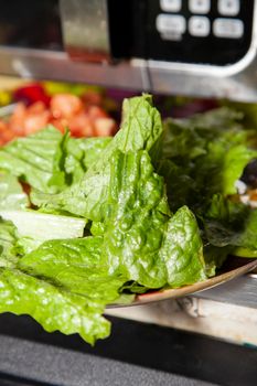 Fresh salad made from romaine lettuce and diced tomato in front of a microwave