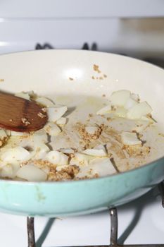 Stir-frying cut yellow onion and diced roasted garlic in a blue pan