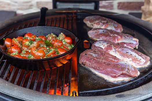 Duck breast on the grill and a skillet with tomatoes and fire beneath