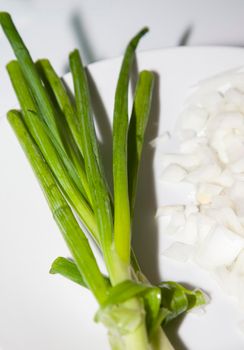 Whole green onion bulbs on a white plate along with diced yellow onion