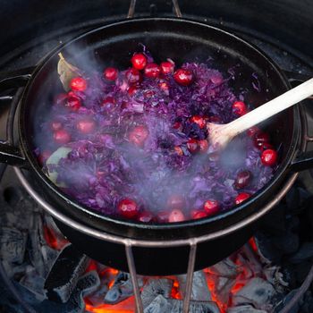 Making red cabbage with cranberries in a dutch oven on a barbecue with fire beneath