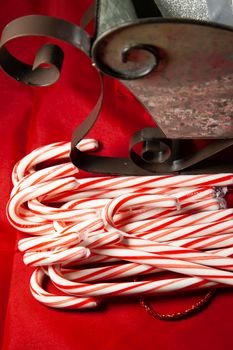 Candy canes on a red, Christmas background with a tin sleigh filled with silver presents in the background