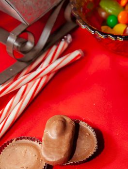 Candy canes and multicolored candies in a bowl on a red tabletop with a sleigh in the background