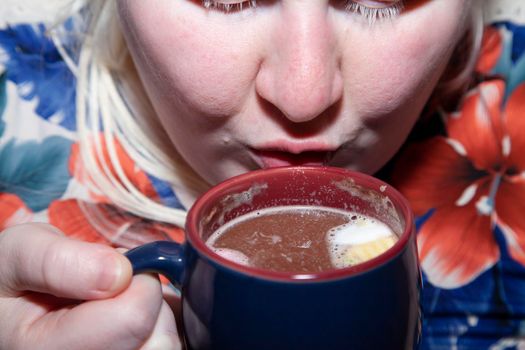 Woman drinking hot cocoa from a blue and red mug slowly