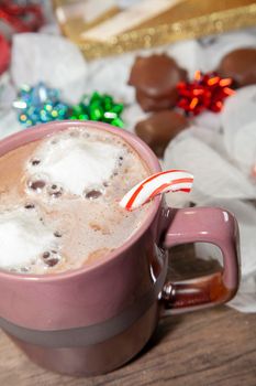 Hot cocoa with melted marshmallows and a broken candy cane, with blue, green, and red bows, pecan and caramel candies, and a gold package