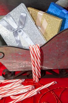 Silver sleigh filled with silver, gold, blue, and red gifts on a red table top next to candy canes