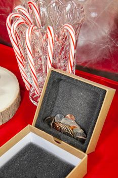 Empty, unwrapped gift box filled with pennies, nickels, dimes, quarters, and a dollar coin, on a red table top with candy canes in the background
