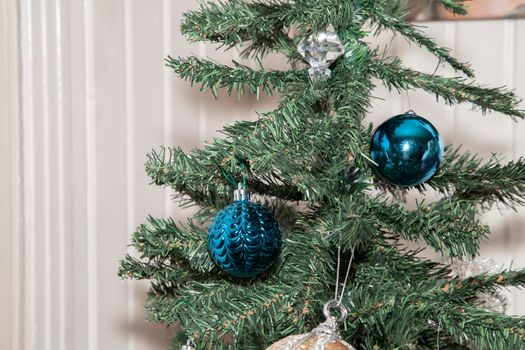 Blue globes hanging on an artificial Christmas tree near a clear and a tan decoration