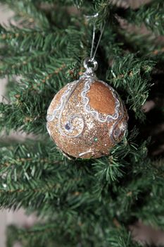 Large, fluffy tan and silver holiday ornament on an artificial green Christmas tree