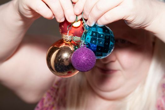 Woman preparing to hang red poinsettia, gold, purple, and blue globes for the holidays