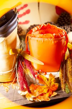 A hunter orange pouch on a wooden slab next to orange and red berries and leaves between boots with pinecones and red hand turkeys in the background in yellow frame