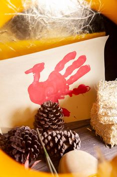 Red hand turkey on vanilla construction paper with hay and pinecones, in a yellow frame, with a golden tone