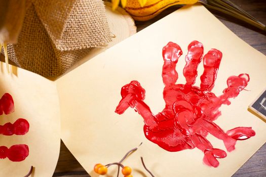 Red hand turkey on vanilla construction paper with orange berries and fall foliage on it and burlap in the background
