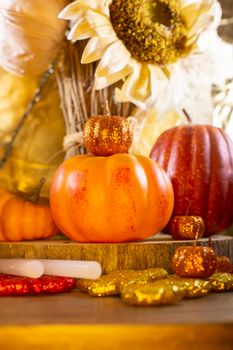 Small orange pumpkins, small red pumpkin, small orange glitter pumpkins, red, yellow, and orange glitter leaves, glue sticks for crafting, and dried sunflowers against a golden background