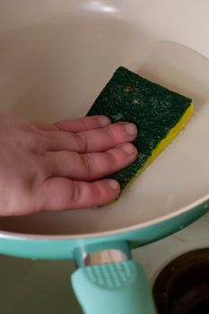 Woman washing a frying pan with a scrubbing sponge