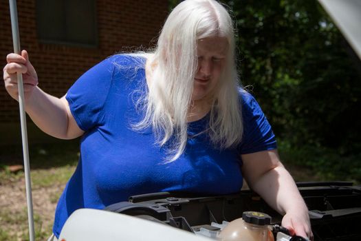 Blind woman checking under the hood of an automobile near the coolant reservoir