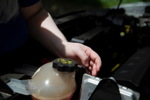 Woman checking under the hood of an automobile near the coolant reservoir