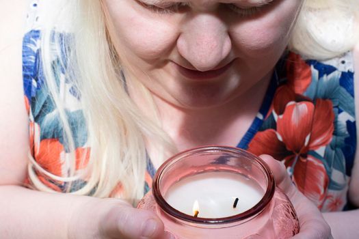 Albino woman enjoying the scent of a lit peach-colored candle