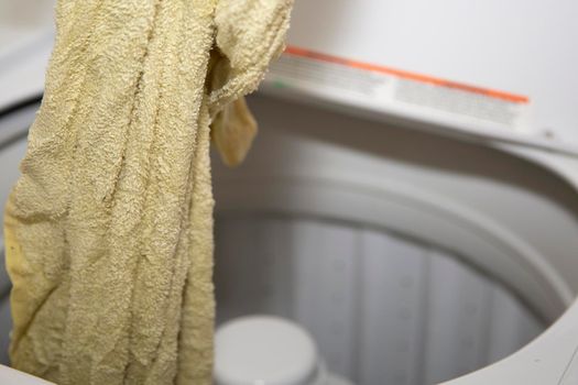 Wet yellow towel being removed from a washing machine