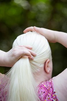 Woman gathering her long, white hair into a ponytail