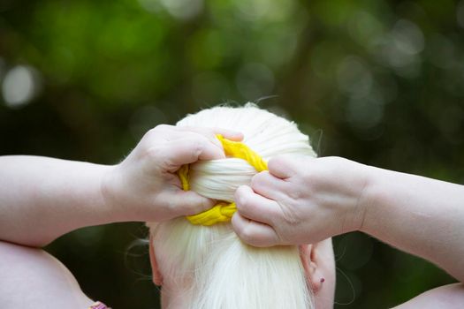 Woman wrapping her long, white hair into a yellow scrunchie