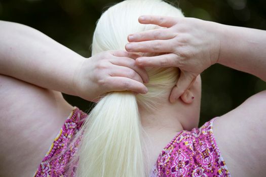 Woman gathering her long, white hair into a ponytail