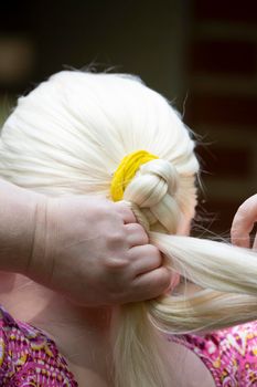 Woman braiding her long, white hair into a ponytail