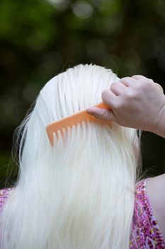 Woman combing long, white hair before styling outdoors