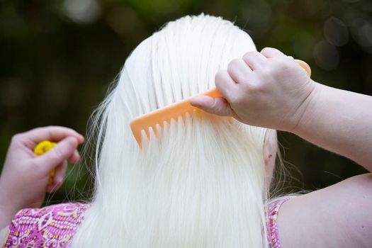 Woman combing long, white hair before styling outdoors