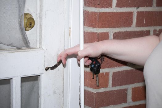 Woman holding keys and reaching for a screen door handle