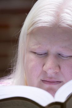 Legally blind albino woman reading a book outside
