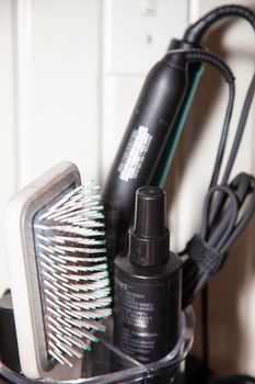 Hair brush with hair in it, spray, and styling tools with a light switch in the background